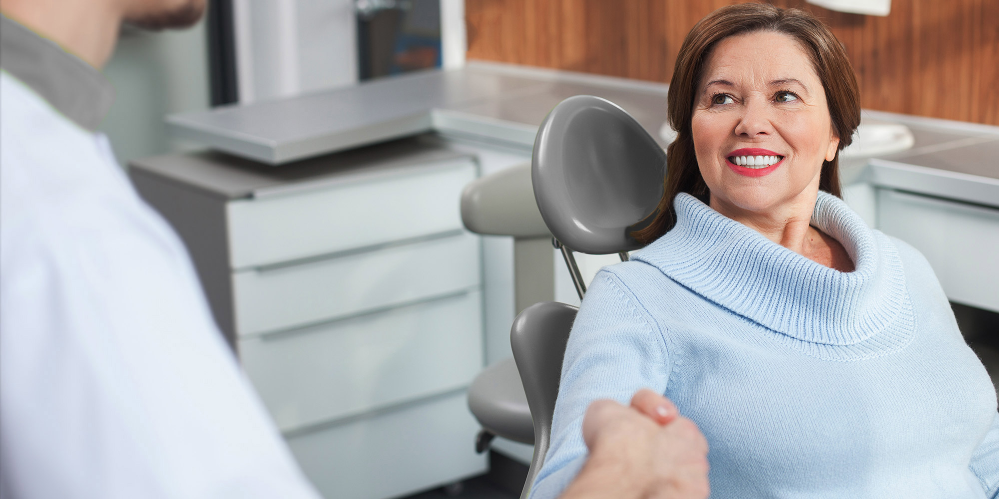 Very nice lady in dental chair smiling looking at doctor shaking his hand.