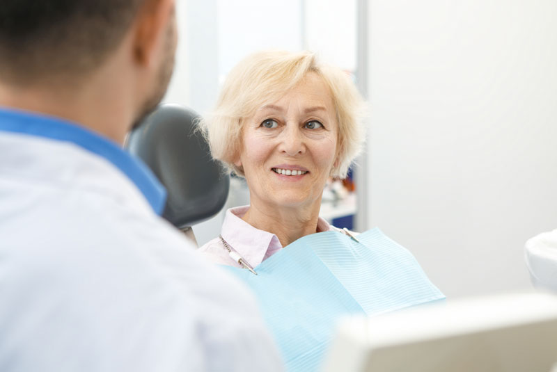 a dental patient smiling as she sits in a chair with a periodontist facing her before she gets treated with crowns and bridges.